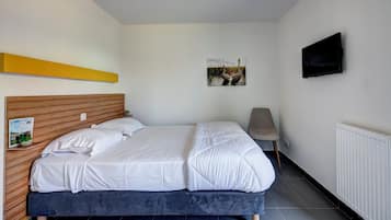 Un dormitorio con cabecera de madera, cama con ropa de cama blanca, mesita de noche con una planta, un cartel en la pared y un televisor montado en la pared.