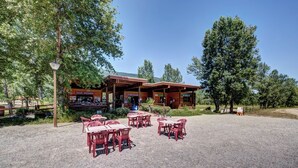 A rustic wooden building with a covered patio area, outdoor seating, and informational signage. - Vacancéole Les Chambres des Oiseaux (Motz)