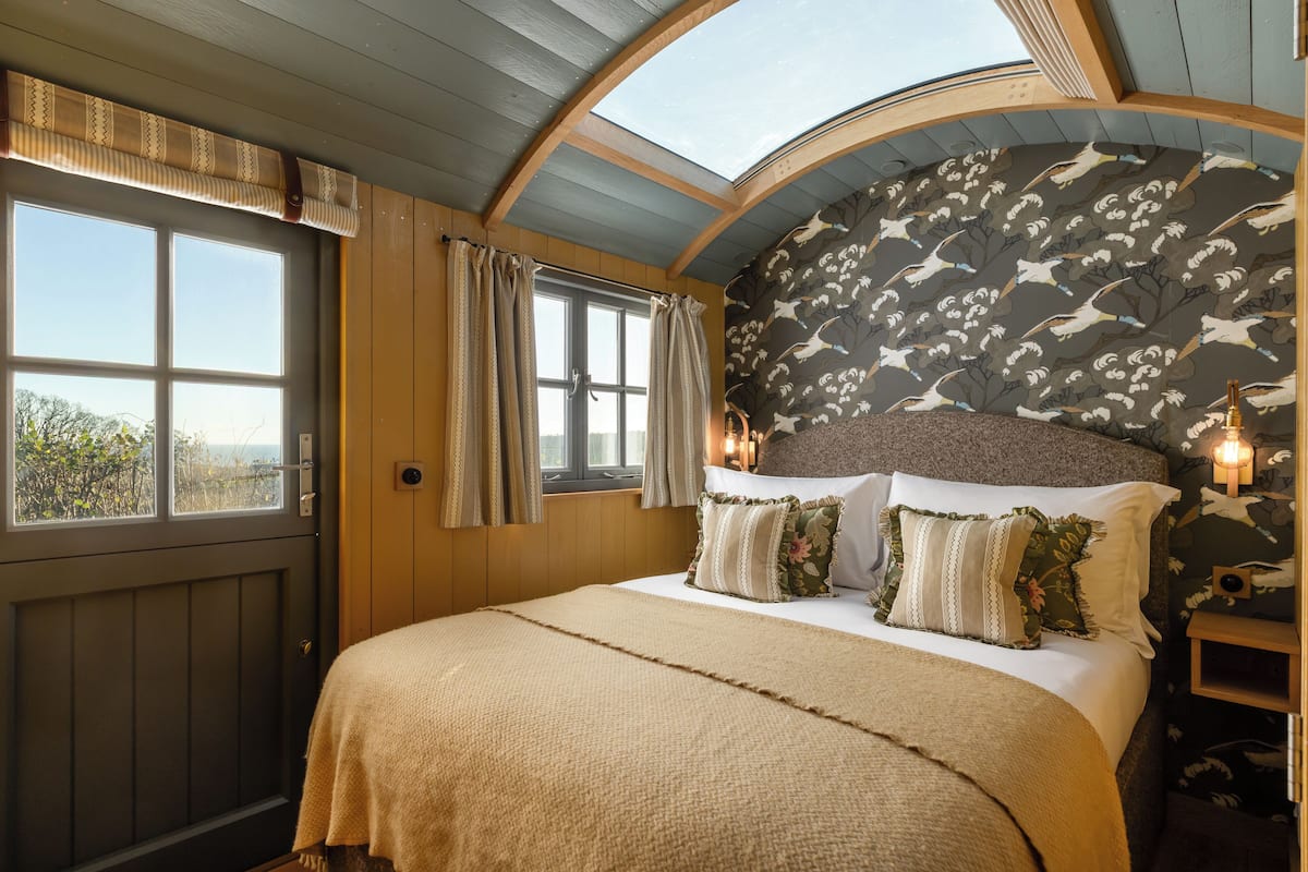 Ein Schlafzimmer mit einem großen Bett, einem Oberlicht, einem Fenster mit Vorhängen und einer Wand mit Vogelmotiv.