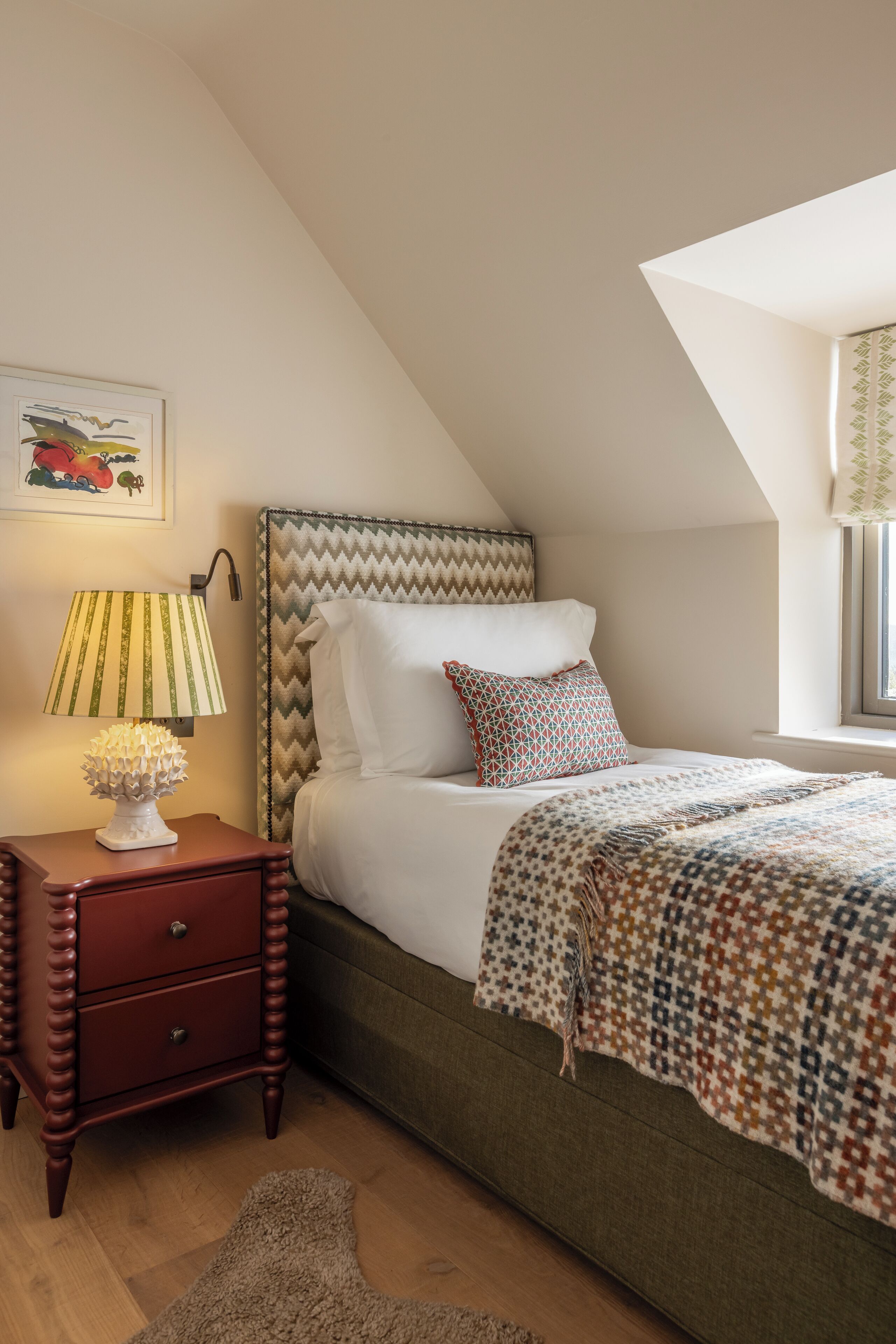 A bedroom with a bed, a nightstand, a lamp, and a window with curtains.