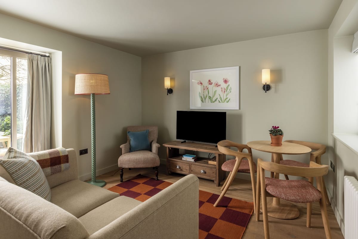 Ein Wohnzimmer mit Sofa, Sesseln, Fernseher und einem kleinen Tisch mit Stühlen.