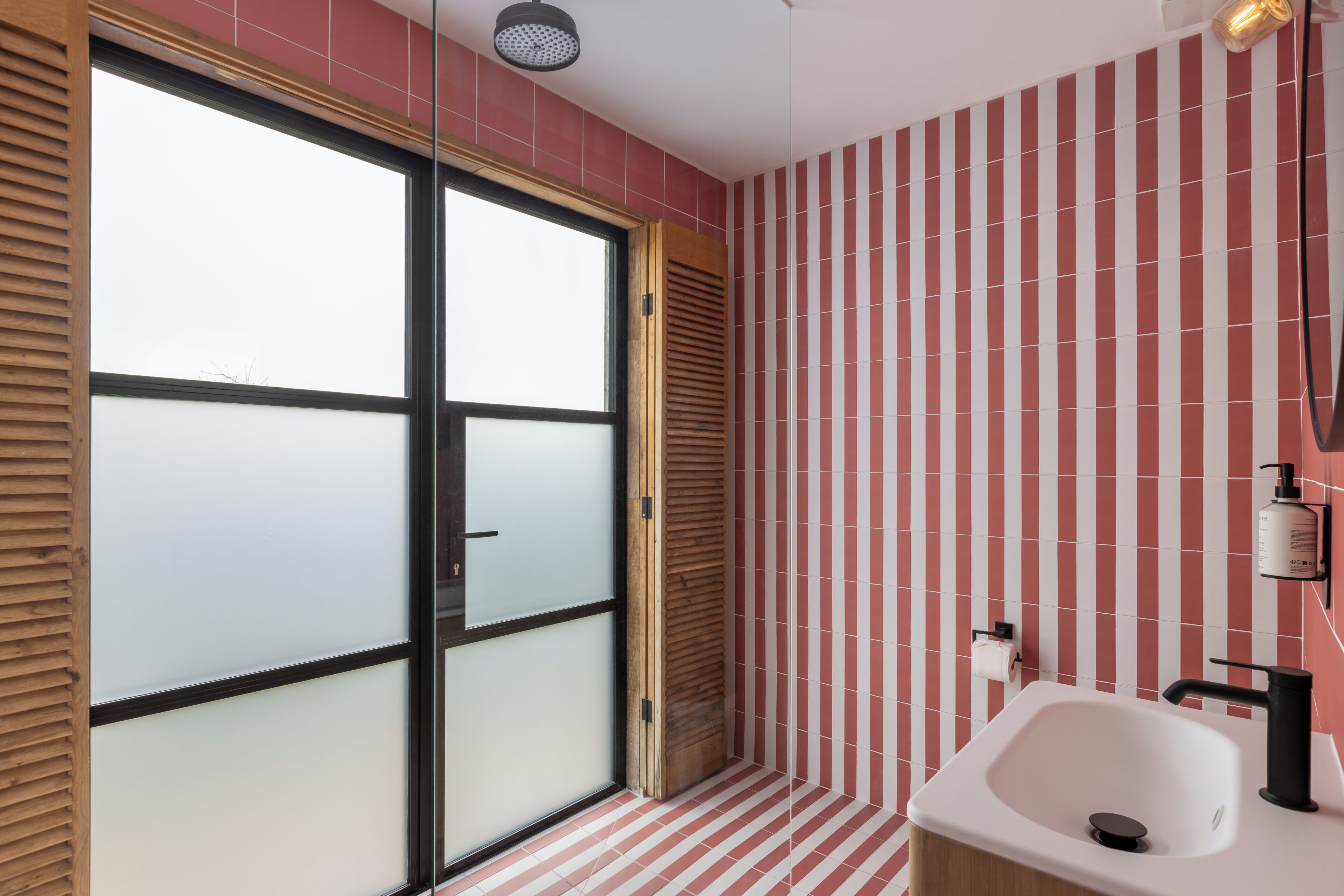 A bathroom with a large glass door, a white sink, and a striped tile wall.