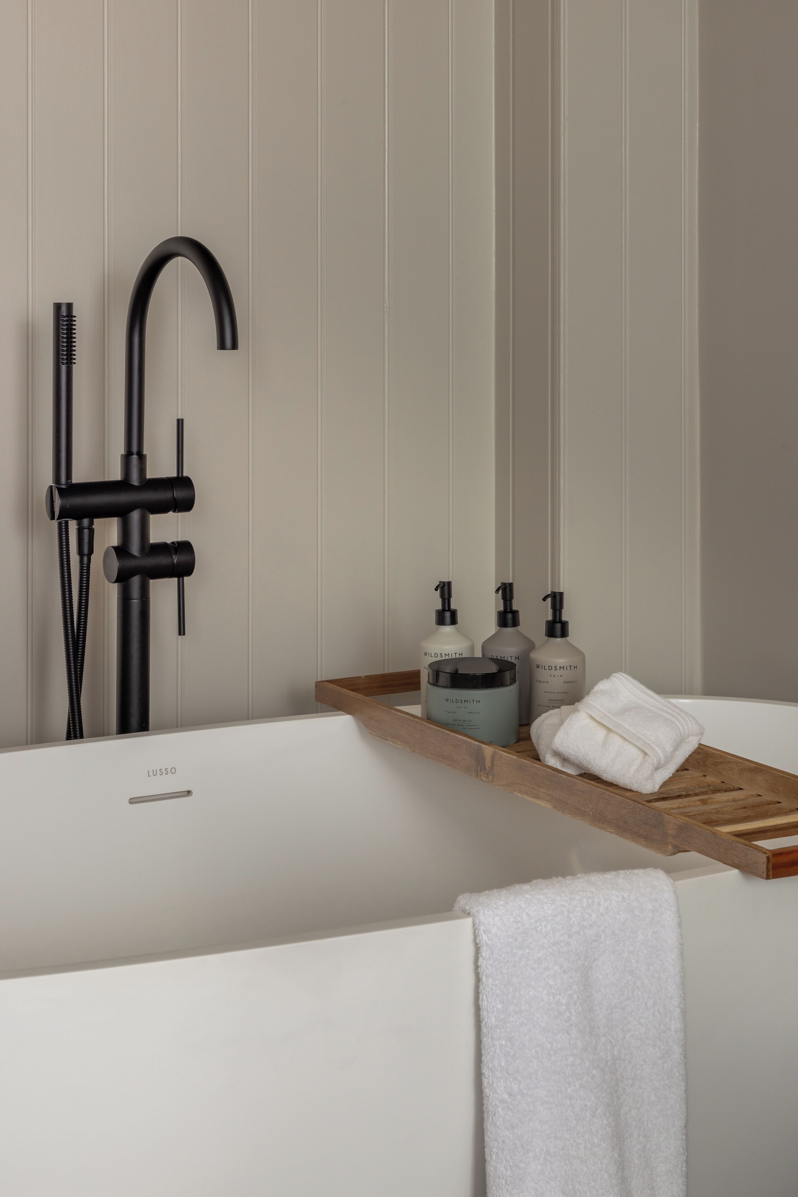 A modern bathroom with a bathtub, a black faucet, and a wooden shelf with toiletries.