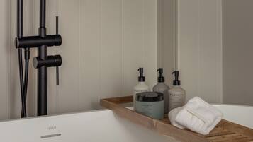 A modern bathroom with a bathtub, a black faucet, and a wooden shelf with toiletries.