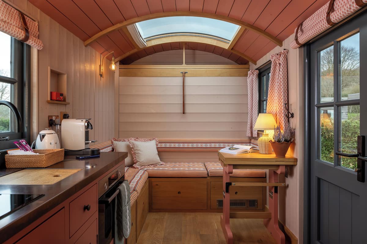 Eine kleine Küche mit integriertem Sitzplatz, einem Tisch mit Lampe und einem Fenster mit Vorhängen.