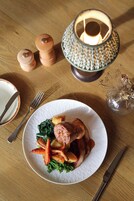 A wooden table with a plate of food, a candle, salt and pepper shakers, and a glass vase with dried flowers.