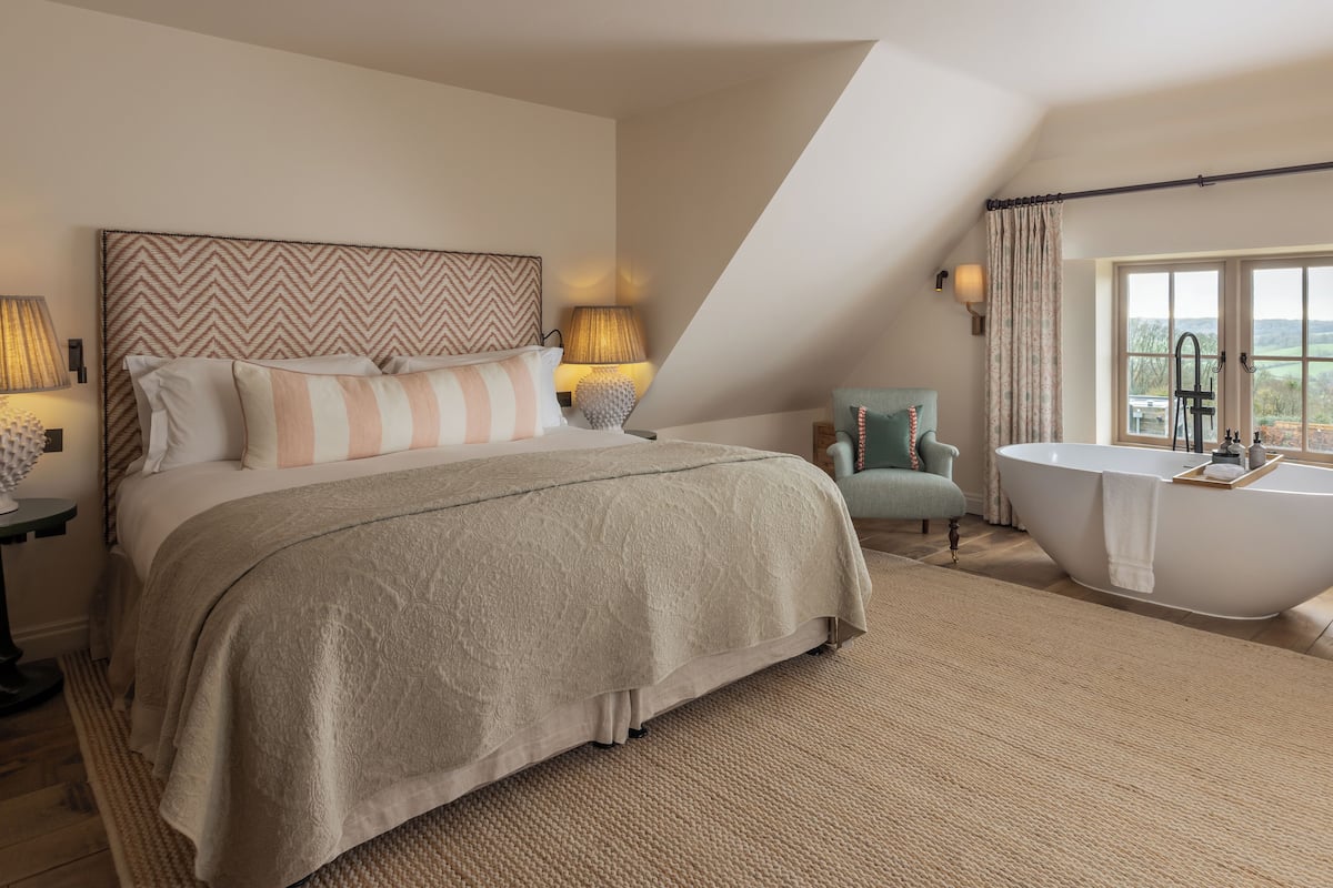 Ein Schlafzimmer mit einem großen Bett, einer Sitzecke mit einem Sessel, einer Badewanne und Blick ins Freie.