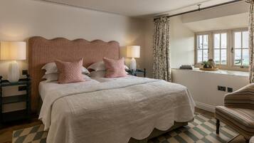 A neatly arranged bedroom with a large bed, two bedside tables, a chair, and a window with curtains.