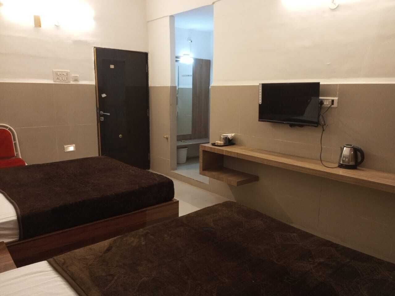 Una habitación pequeña y funcional con dos camas, un televisor en la pared y una repisa con hervidor.