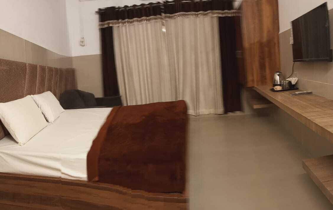 Habitación de hotel con cama, escritorio, silla, ventana con cortinas y televisor de pantalla plana en la pared.