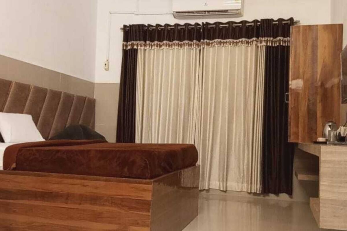 A bedroom with a bed, a wooden headboard, a TV, and a window with curtains.