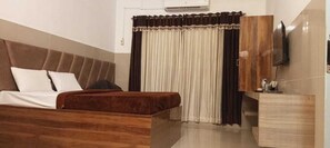 Un dormitorio con cama, cabecera de madera, televisor y ventana con cortinas.