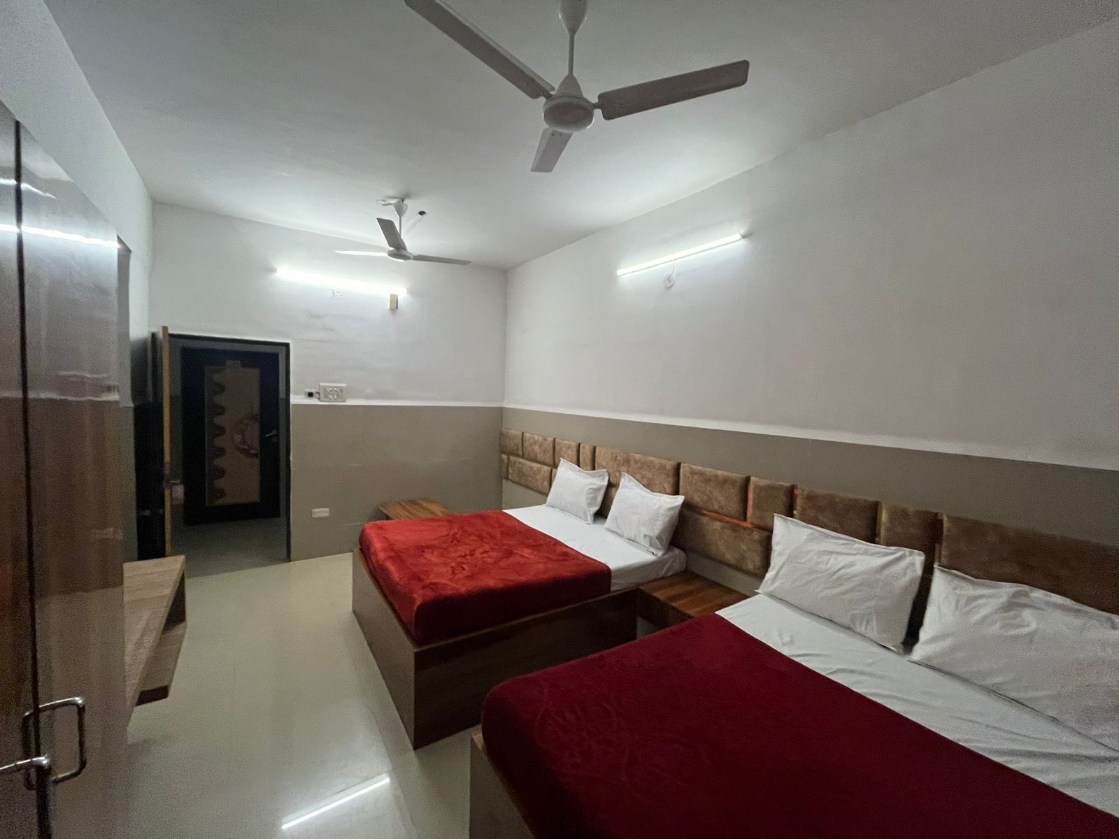 Habitación de hotel con dos camas, cabecero de madera, manta roja y ventiladores de techo.