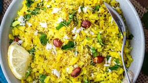 A bowl of yellow rice garnished with herbs and nuts, accompanied by a lemon wedge and a glass of a brownish drink. - HOTEL CRAZY HOME AND RESORT (Jalgaon)