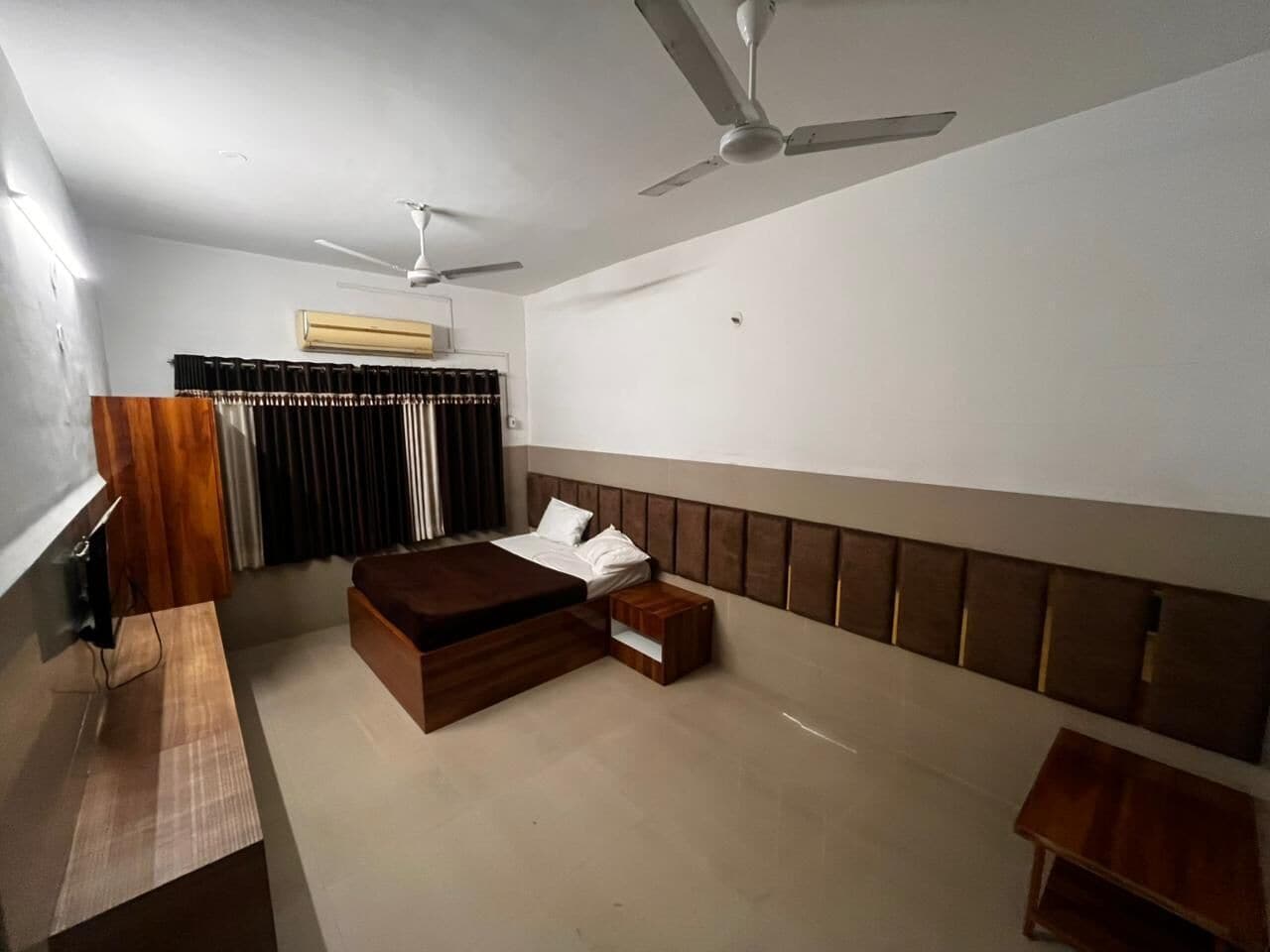 A bedroom with a bed, a wooden nightstand, a ceiling fan, and a window with curtains.
