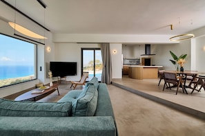 A modern living room with a large sofa, a flat-screen TV, and a dining area with a table and chairs. - Comfortbnb- Theasis Suite with private pool, Sitia (Roussa Ekklisia)