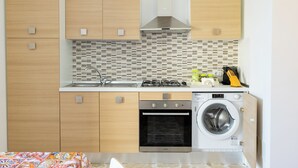 Eine moderne Küche mit Holzschränken, einer gefliesten Spritzschutzwand, einem Gasherd, einem Backofen und einer integrierten Waschmaschine.