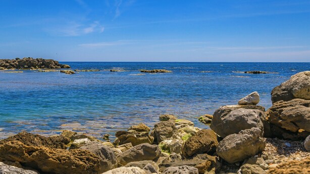 Eine felsige Küstenlinie mit klarem, blauem Wasser und einer entfernten Landmasse.