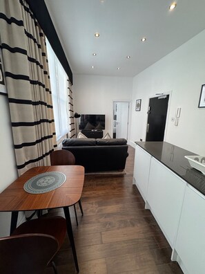 A modern kitchen with a dining area, a black sofa, and a TV. - Clockwork Stay (London)