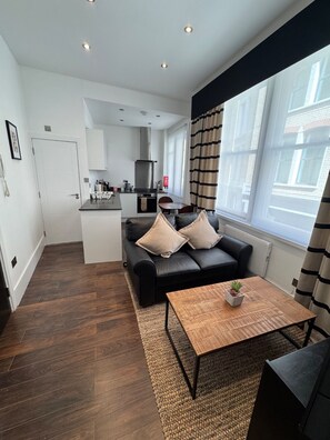 A compact living space with a kitchenette, a sofa, a coffee table, and a view of the outside. - Clockwork Stay (London)