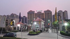 A hotel entrance with a gated driveway, a small pavilion, and multiple flags. - OMAXE DG HOMESTAY (prayagraj)
