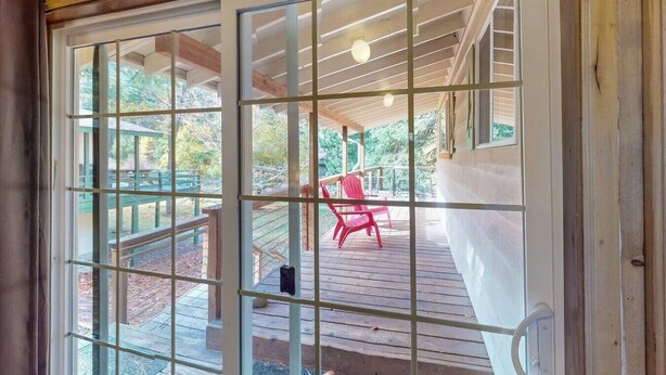 Una terraza de madera con una silla roja, un área cubierta y vista a un paisaje verde.