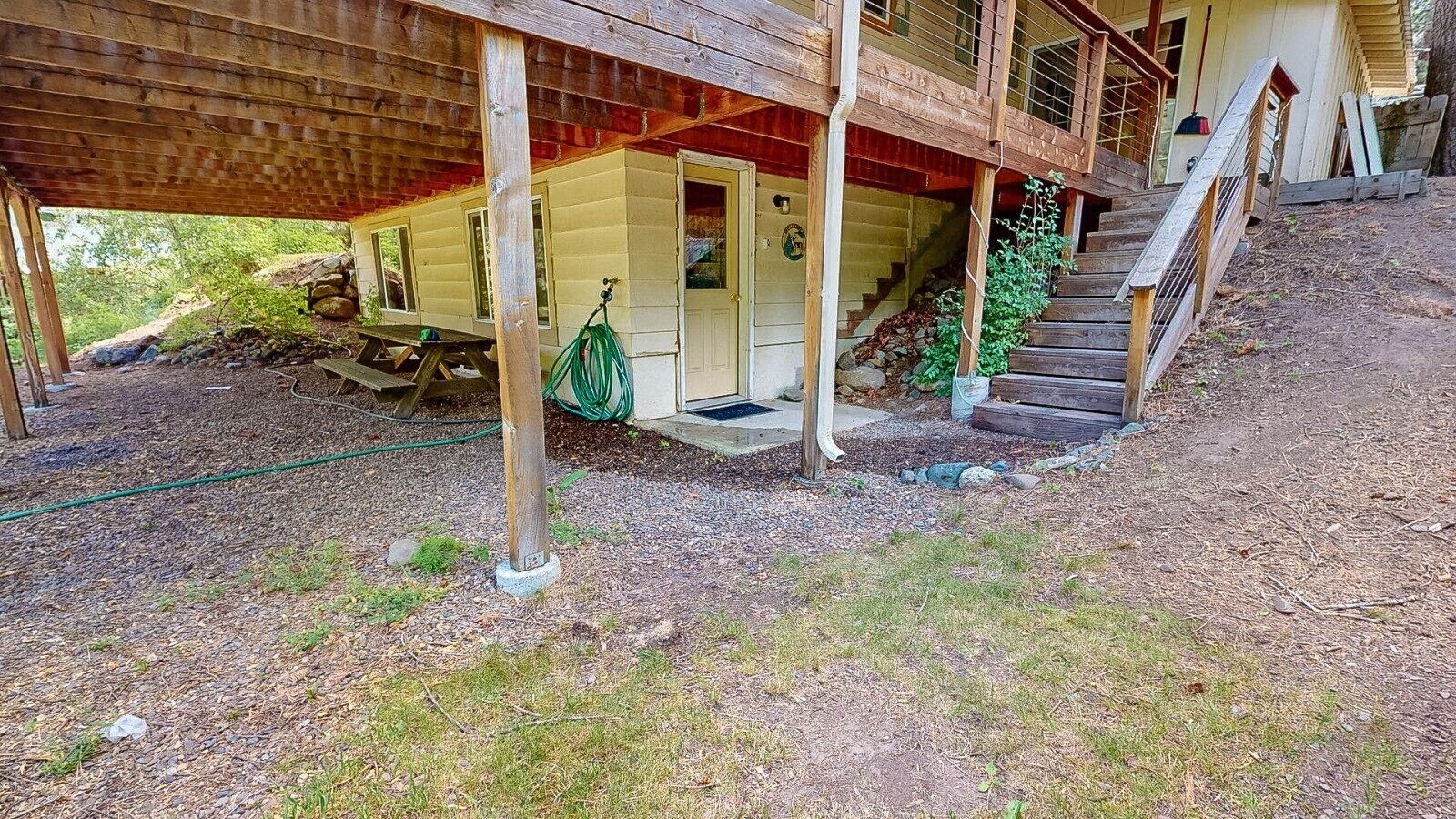 Une cabane en bois dotée d’un porche couvert, d’un escalier menant à une porte et d’un jardin agrémenté de paillis et de gazon.