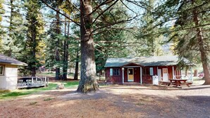 A rustic cabin with a porch, surrounded by trees. - Cozy Frances Lake Retreat | Wallowa Lake Fun (Joseph)