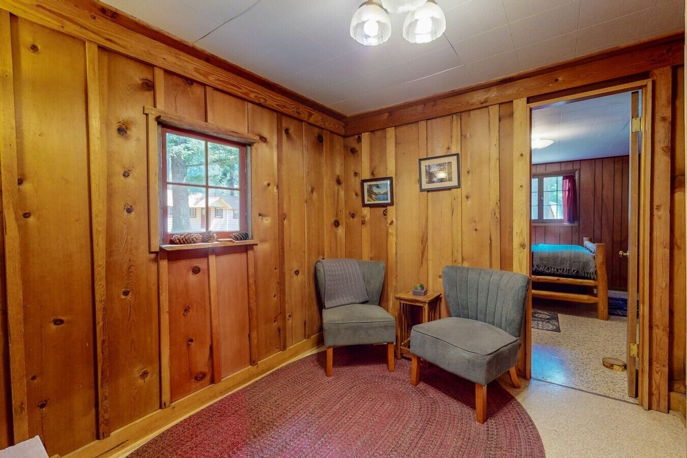 A wooden-paneled room with two armchairs, a small table, and a window with pinecones.