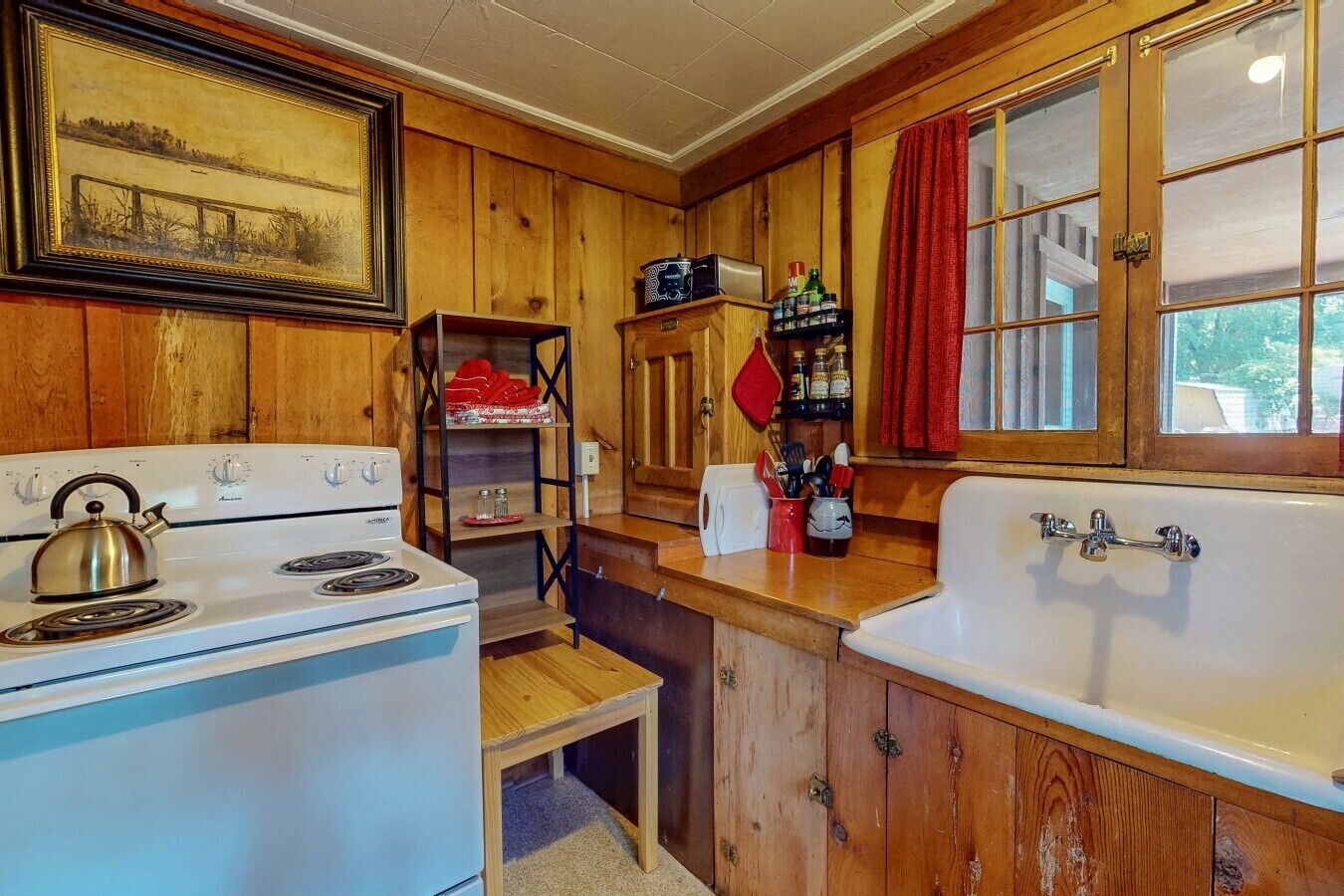 Una cocina con armarios de madera, una estufa, un fregadero y un ventanal con cortinas.