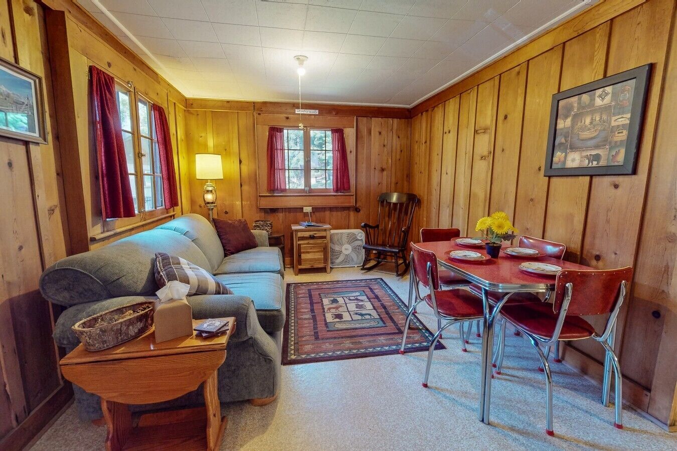 A cozy room with a sofa, a small table, a dining table with chairs, and a window with curtains.
