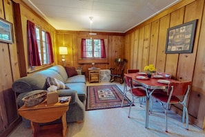 Una habitación acogedora con sofá, una mesita, una mesa de comedor con sillas y una ventana con cortinas.