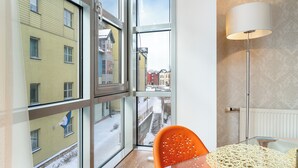 Ein Zimmer mit großen Fenstern, einem Tisch, einem Stuhl und einer Stehlampe.