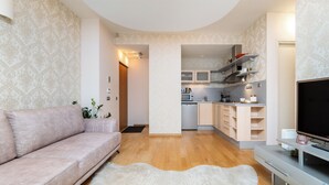 Ein modernes Wohnzimmer mit einer Couch, einem Flachbildfernseher und einer Küchenzeile mit Schränken und Geräten.