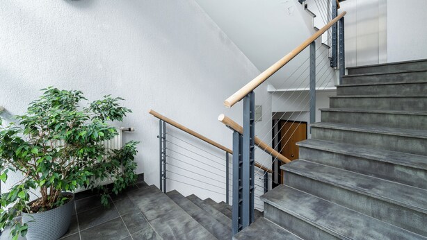 Eine Treppe mit hölzernen Geländern, einem Blumentopf und einer weißen Wand mit einer Leuchte.