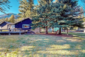 A cabin with a deck, surrounded by trees and a mountain backdrop.