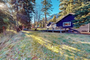 A cabin with a deck, surrounded by trees and mountains.