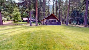 Un lodge con facciata in legno, circondato da alberi alti e un prato curato.