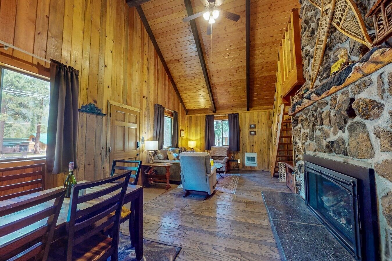 Interior de una cabaña de madera con chimenea, ventilador de techo y pared de piedra.