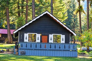 A wooden cabin with a gabled roof, a front door, and a porch with a railing.