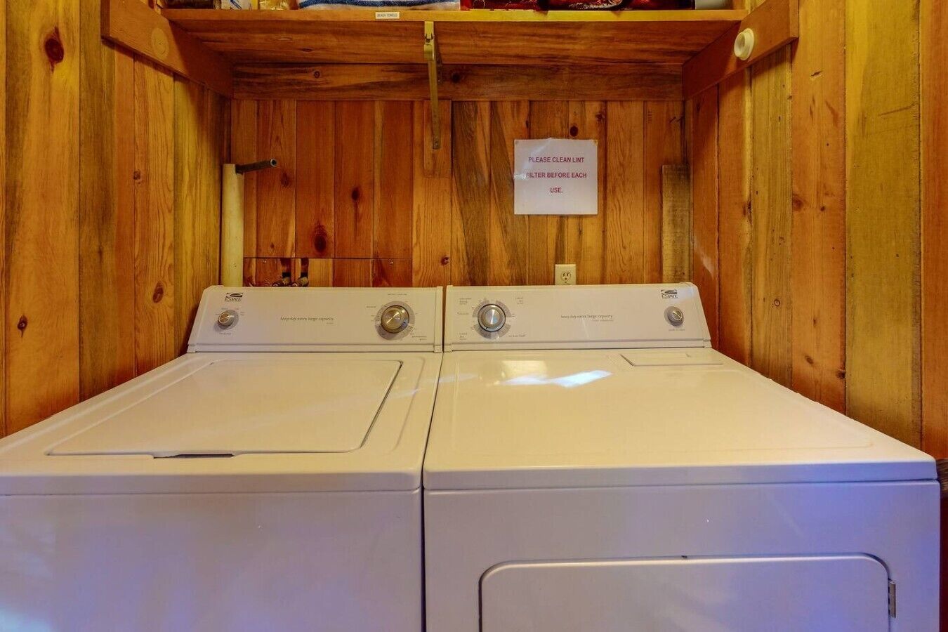 A laundry room with two white front-loading washers and a sign instructing to clean the lint filter before each use.