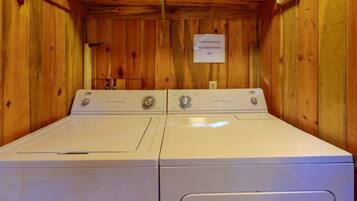 A laundry room with two white front-loading washers and a sign instructing to clean the lint filter before each use.