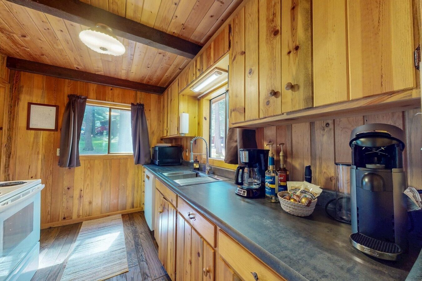 A wooden cabin interior with a kitchenette, including a stove, microwave, coffee maker, and a coffee pot.