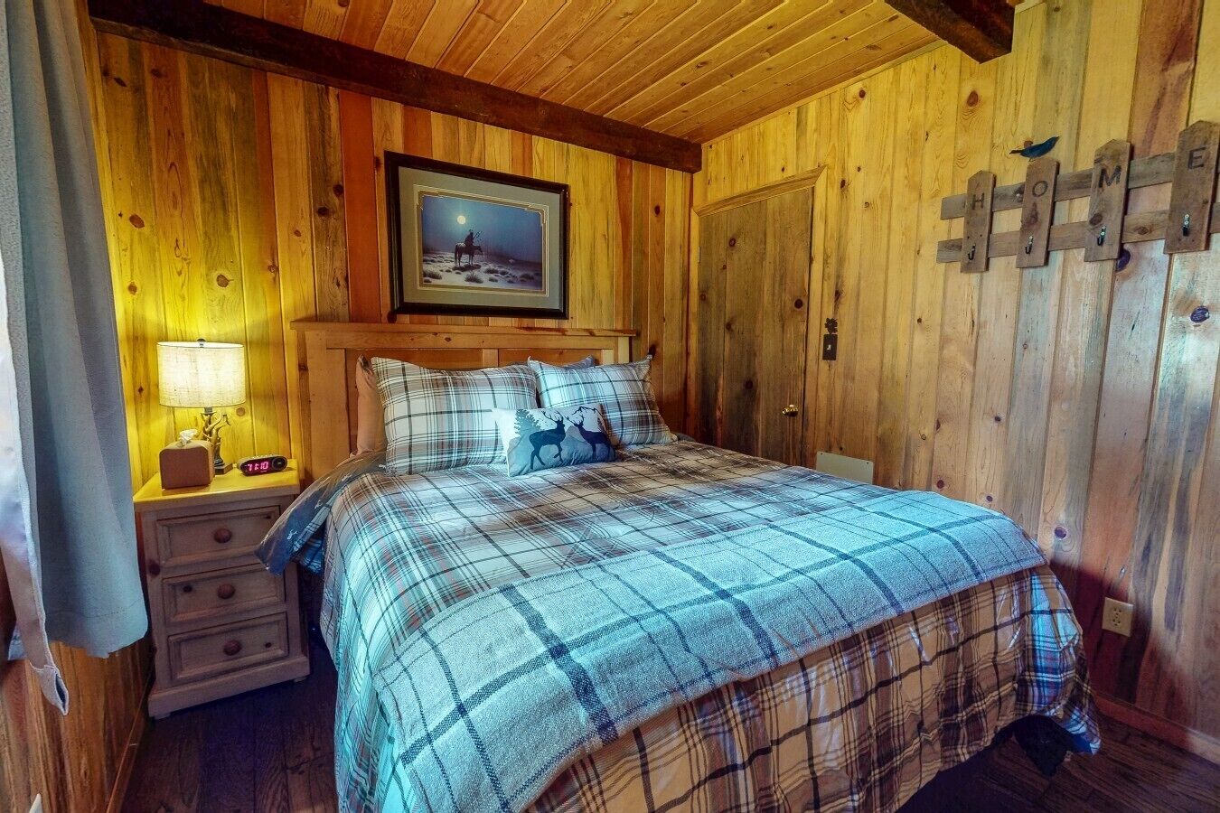 Une chambre à coucher dans un chalet en bois, avec une couverture à carreaux sur le lit, une table de chevet avec une lampe et un tableau encadré au mur.