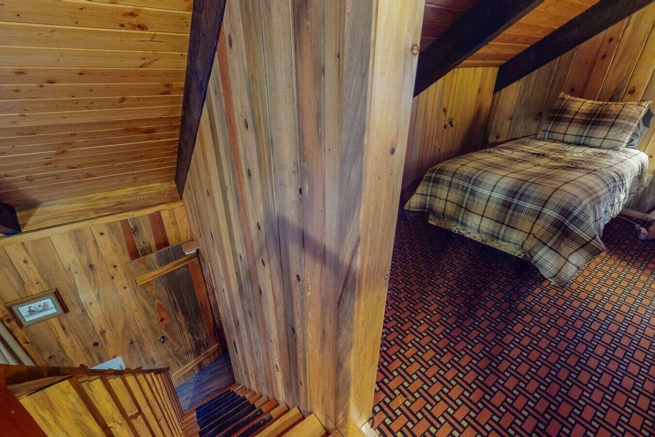 Een houten interieur met een bed, een vloer met een patroon en een klein, ingelijst beeld aan de muur.