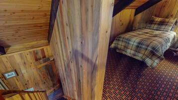 Een houten interieur met een bed, een vloer met een patroon en een klein, ingelijst beeld aan de muur.