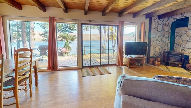 Un salón amplio con techo de madera, puertas correderas de vidrio que dan a una terraza, un televisor y una chimenea de piedra.