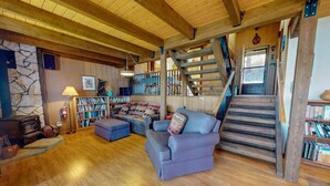 Un interior de madera con chimenea, estanterías, un sofá y una escalera.