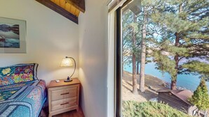 Un dormitorio con una cama, una mesita de noche, una lámpara y una ventana con vistas a árboles y un muelle.