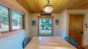 Uma sala de jantar com uma mesa e cadeiras de madeira, uma janela com vista para árvores e teto de madeira.